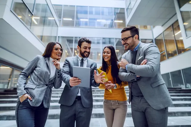 four-successful-smiling-businesspeople-standing-front-corporate-building-looking-tablet-that-man-middle-holding